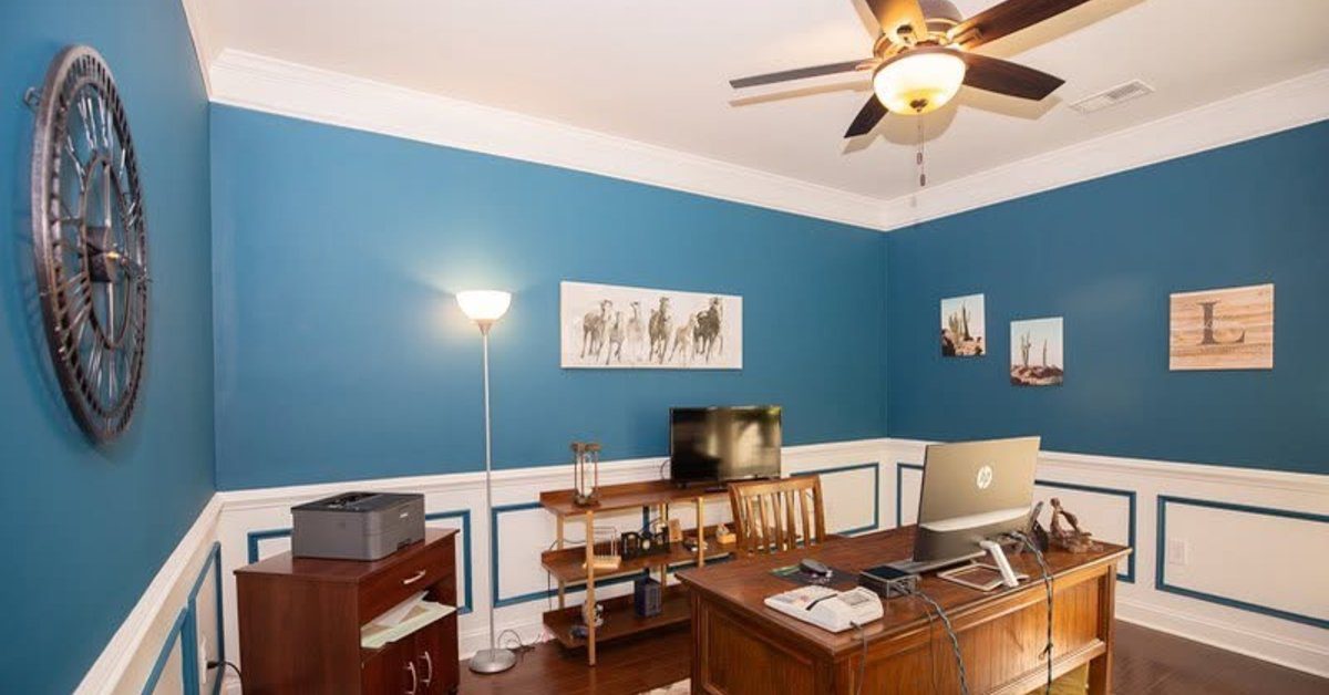 A freshly painted home office with blue accent walls, white trim detailing, wood furniture, and a desk.