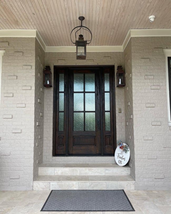 Covered entry features a dark wood and frosted-glass front door, matching sidelights, brick walls, and three lanterns.