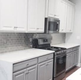 Bright kitchen with white cabinetry, gray subway tile backsplash, pale countertops, and stainless range and microwave.