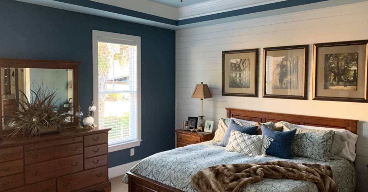Spacious bedroom featuring a wooden bed, blue walls, framed artwork, matching dresser, and a ceiling fan overhead