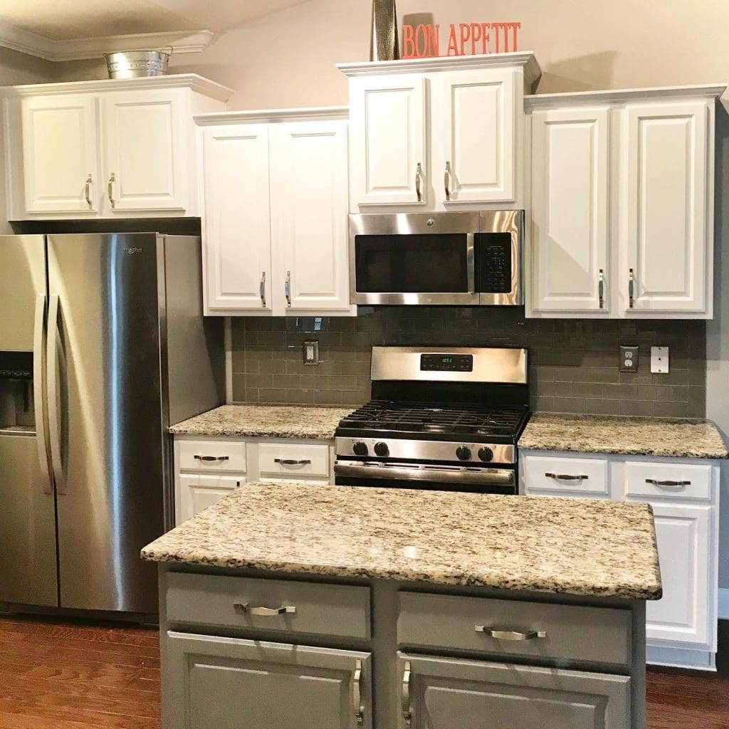 White cabinets, stainless steel appliances, granite counters, and a gray island fill a remodeled kitchen.