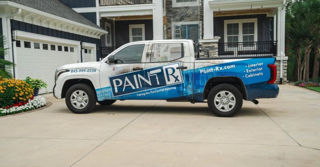 Paint-Rx branded pickup truck parked outside a large blue and white home with painting work underway.
