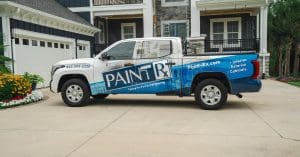 Paint-Rx branded pickup truck parked outside a large blue and white home with painting work underway.