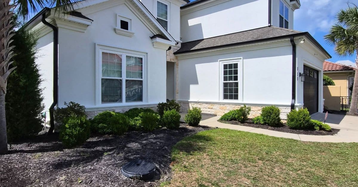 Fresh white exterior with dark gutters and stone detailing frames a two-story home surrounded by neat landscaping.
