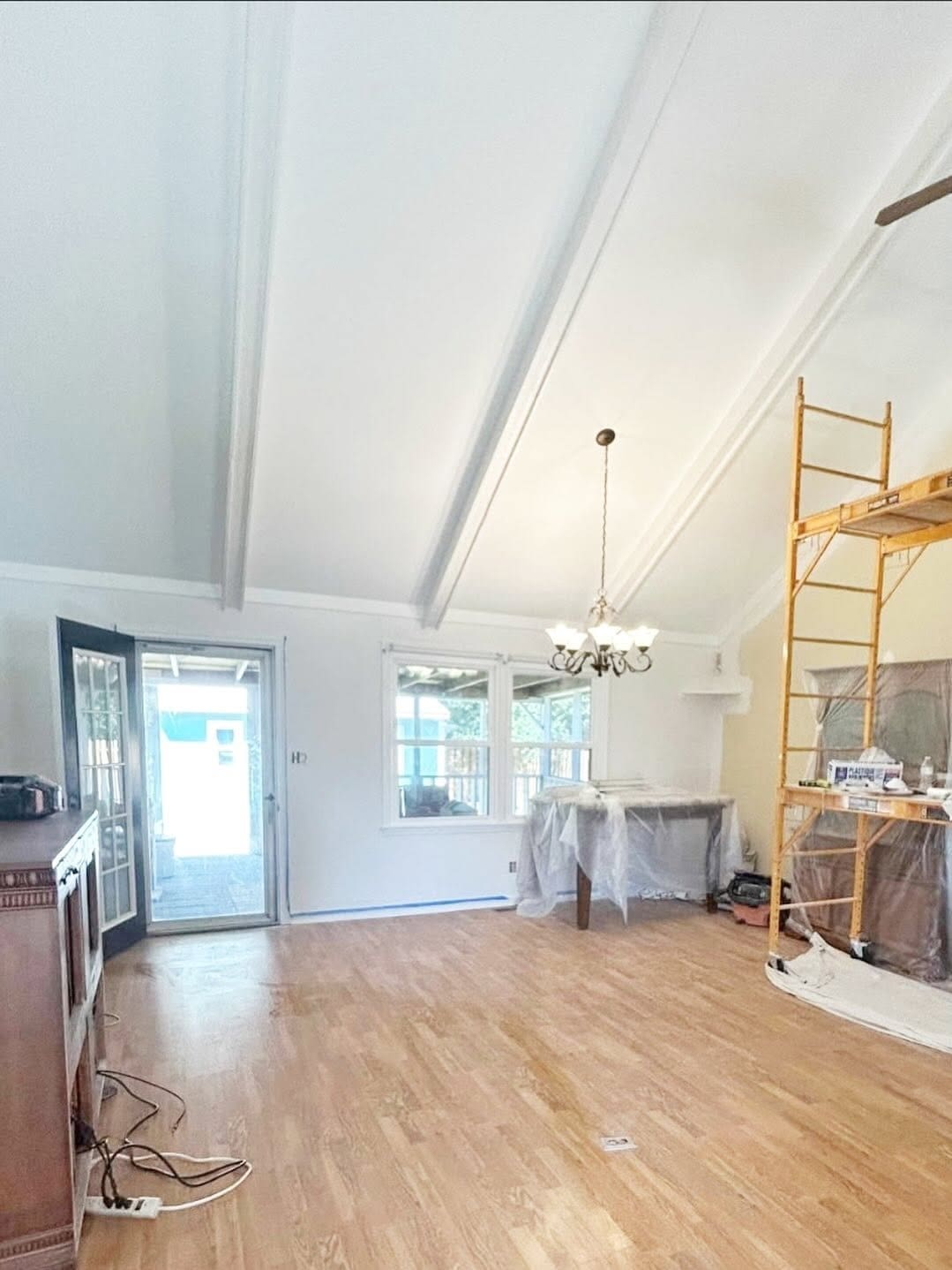 Interior renovation with scaffolding, covered furniture, white vaulted ceilings, wood flooring, and a chandelier.