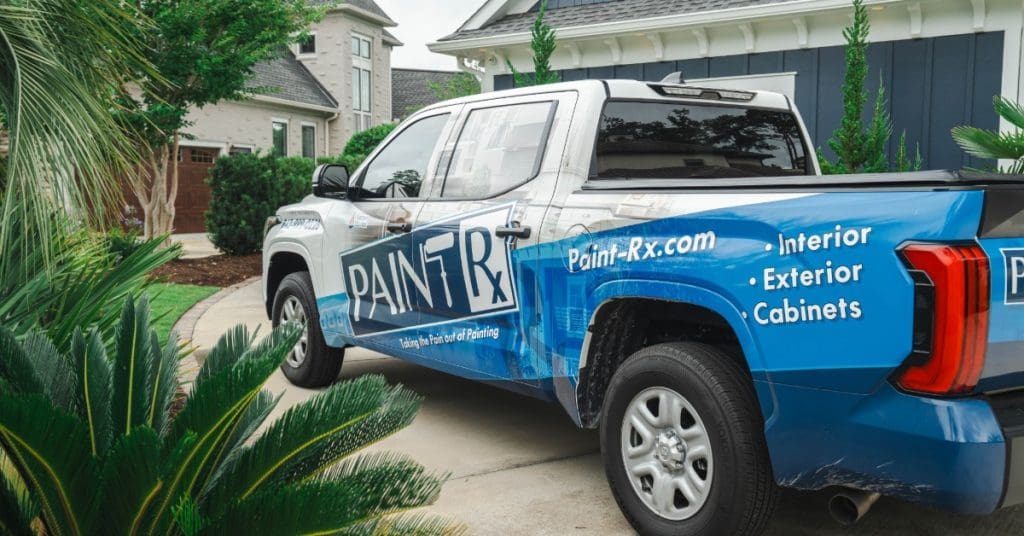 A blue and white Paint Rx pickup truck parked in a residential driveway, advertising interior and exterior painting.